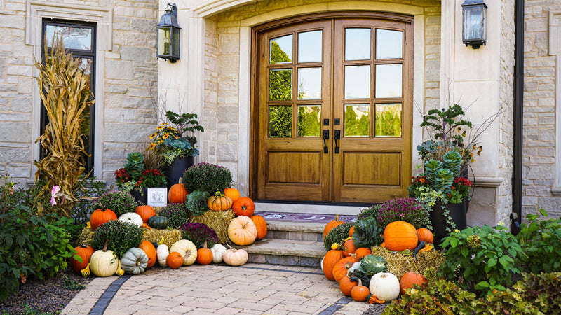 Signature fall porch display — heirloom pumpkins and hay bales flanking a limestone entry